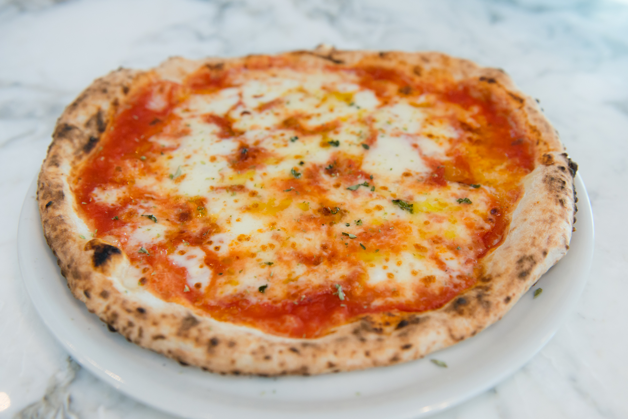 Close up of side angle of our classic margherita pizza made with tomato, fior di latte cheese, oregano and apulian olive oil